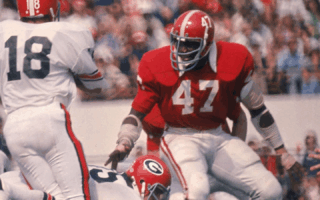 Two football players in action during a game, with one player wearing jersey number 47 in a red uniform and the other in a white jersey number 18.